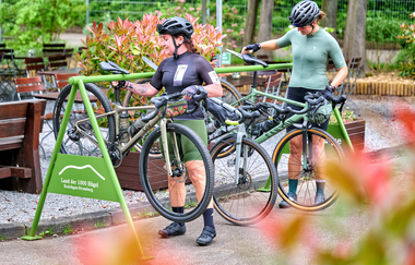 Zwei Gravelbikerinnen hängen ihre Fahrräder an der Hügel-Pause – dem offiziellen Radständer im Land der 1000 Hügel – sicher ein. | © Kraichgau-Stromberg Tourismus e.V. | Florian Trykowski