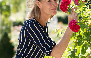 Eine Frau mit Sonnenhut riecht an roten Rosen. | © Björn Hänssler