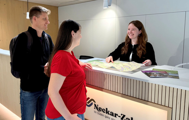 Beratung eines Paares an der Theke der Tourist-Info. Vor den Gästen und der Mitarbeiterin liegt eine Karte und diverse Prospekte. | © Neckar-Zaber-Tourismus e.V.