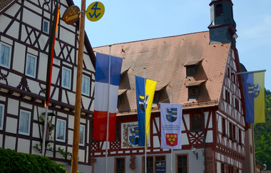 Blick auf das im Fachwerkstil errichtete Rathaus in Freudenberg. Im Vordergrund sind viele Fahnen zu sehen. | © Liebliches Taubertal