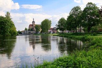 Blick auf die Regiswindiskirche bei blauem Himmel und einem umliegenden Fluss. | © Stadtverwaltung Lauffen am Neckar