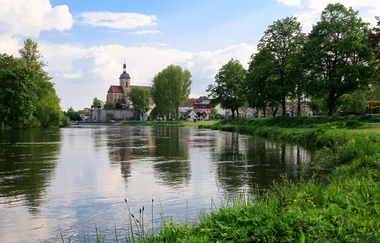 Blick auf die Regiswindiskirche bei blauem Himmel und einem umliegenden Fluss. | © Stadtverwaltung Lauffen am Neckar