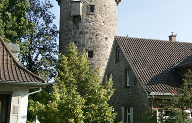 In der Mitte von zwei Häusern in der Roten Turmstraße steht der Rote Turm. Der Fuß des Turmes ist durch einen grünen Baum verdeckt.