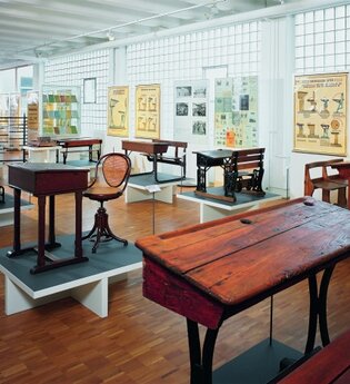 Blick in das Schulmuseum der Firma VS in Tauberbischofsheim. Hier sind alte Schulbänke, Tische und Stühle sowie Wandkarten zu sehen. | © Tourismusverband "Liebliches Taubertal" e.V.