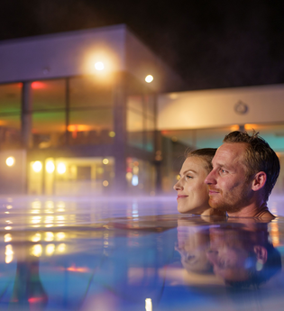 Ein Man und eine Frau sind im Mineralaußenbecken der Therme bei Nacht. | © Björn Hänssler