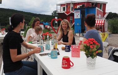 Blick auf mehrere Personen, die vor dem Toppels-Haus "Verdrehte Welt" Getränke zu sich nehmen. Die Tassen stehen ebenfalls auf dem Kopf. | © TOPPELS - Verdrehte Welt