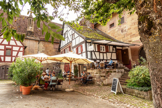 Wagnerhaus Cafe im Klosterhof Maulbronn mit Gästen an Tischen unter Sonnenschirmen, umgeben von historischen Gebäuden und Pflanzen. | © Wagnerhaus Café Maulbronn