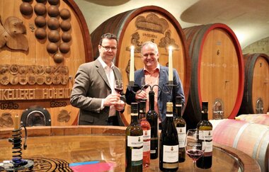 Zwei Männer stehen im Weinkellerer, vorne stehen Weinflaschen und Kerzen brennen | © Touristikgemeinschaft Hohenlohe e. V.