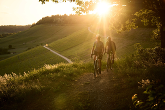 Mann und Frau gravelbiken über die Höhenzüge des Kraichgau-Strombergs. Im Hintergrund Sonnenuntergang. | © Tourimia Tourismus GmbH | Stefan Leitner Photography