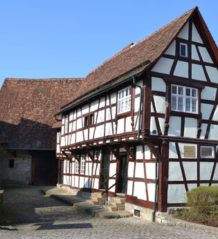 Ein Fachwerkhaus mit weißem Putz und braunen Holzbalken, Steindach und gepflastertem Hof | © Stadt Sinsheim