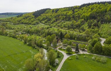 Luftbildaufnahem auf einen Parkplatz/Wohnmobilstellplatz bei Distelhausen. Daneben ist eine Kapelle und ein Friedhof zu sehen.  Es ist ein idyllischer Ort an der Tauber, mit Wiesen und bewaldeten Hügeln. | © Tourist-Info Tauberbischofsheim