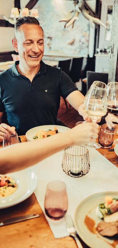 Vier Personen sitzen an gedecktem Tisch und stoßen mit Wein an | © Touristikgemeinschaft HeilbronnerLand | Chris Frumolt 2023