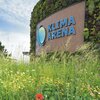 Holzfassade mit dem blauen Schriftzug 'KLIMA ARENA' und einem stilisierten Logo, davor eine Wiese mit Wildblumen und Mohnblumen. | © Landratsamt Rhein-Neckar-Kreis; Foto Dorothea Burkhardt