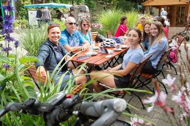 Gruppe von Radfahrern sitzt an einem Holztisch im Freien mit Fahrradhelmen und Fahrrädern im Hintergrund | © Landratsamt Rhein-Neckar-Kreis; Foto Dorothea Burkhardt